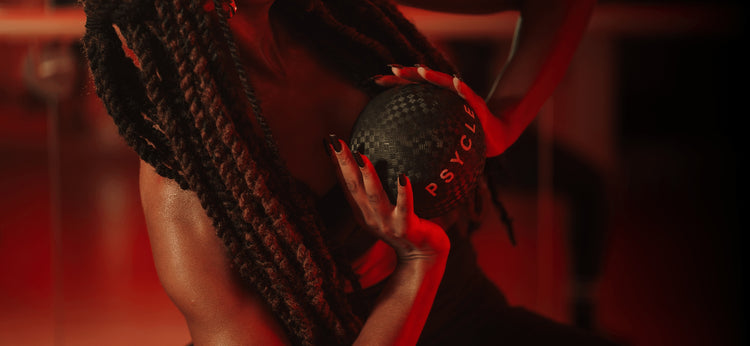 Women with braids bends to the side holding a PSYCLE barre ball
